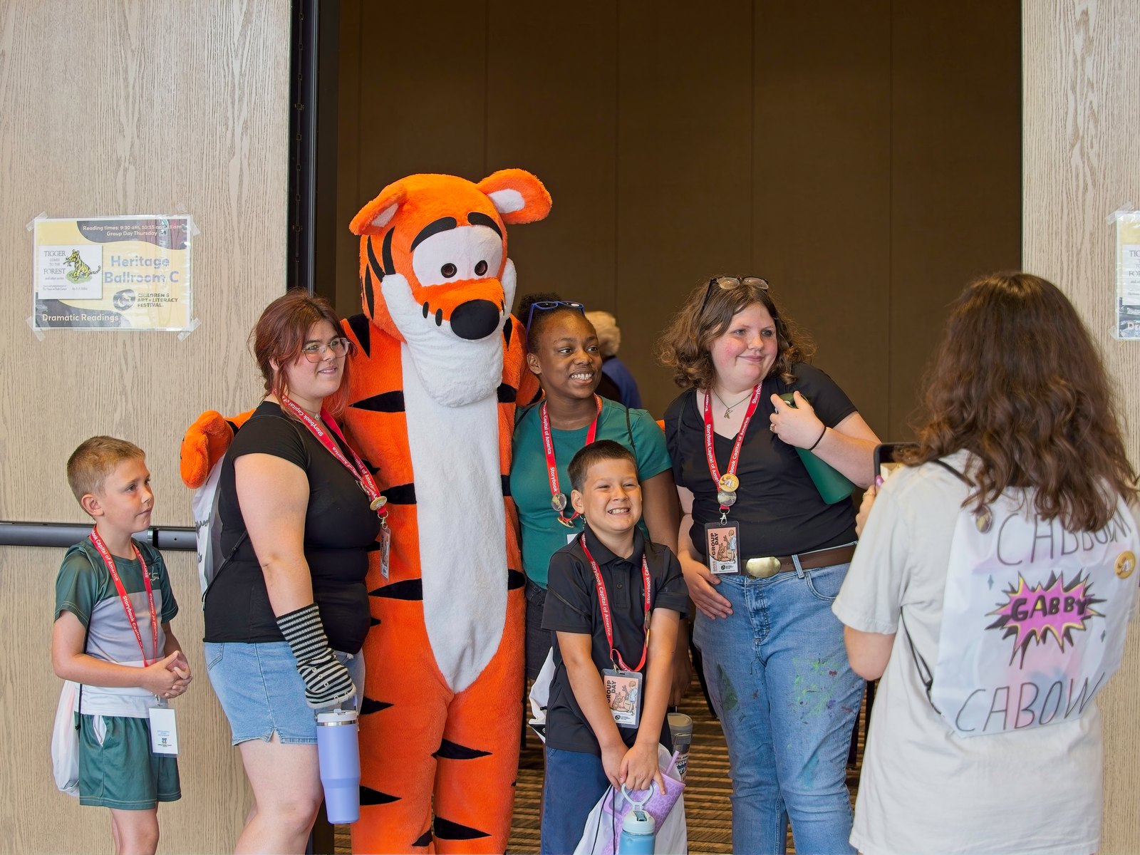 Children and festival volunteers posing with a costumed tiger character at the Children's Art and Literacy Festival