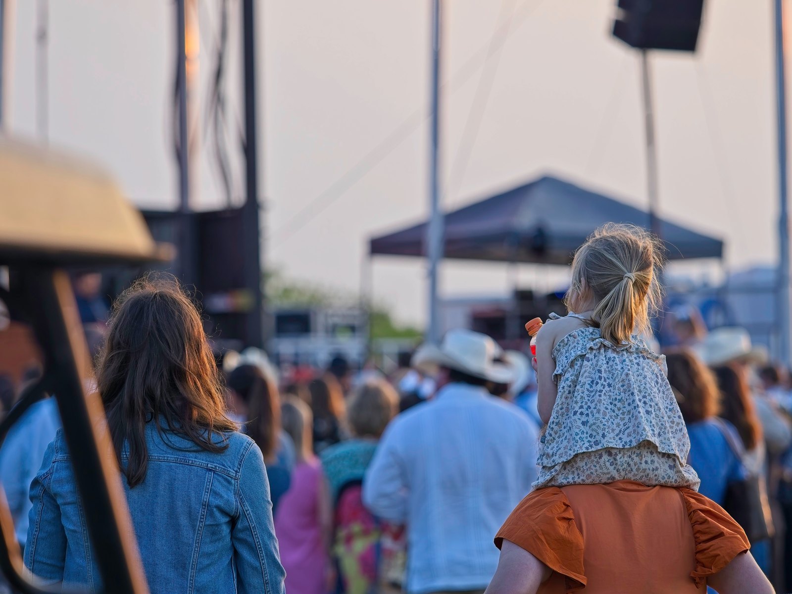 Festival crowd at golden hour with a child riding on a parent's shoulders