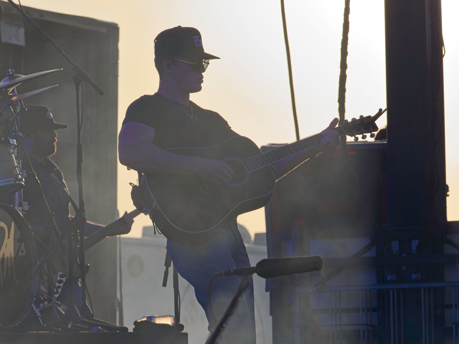 A guitarist silhouetted in hazy backlight on an outdoor stage